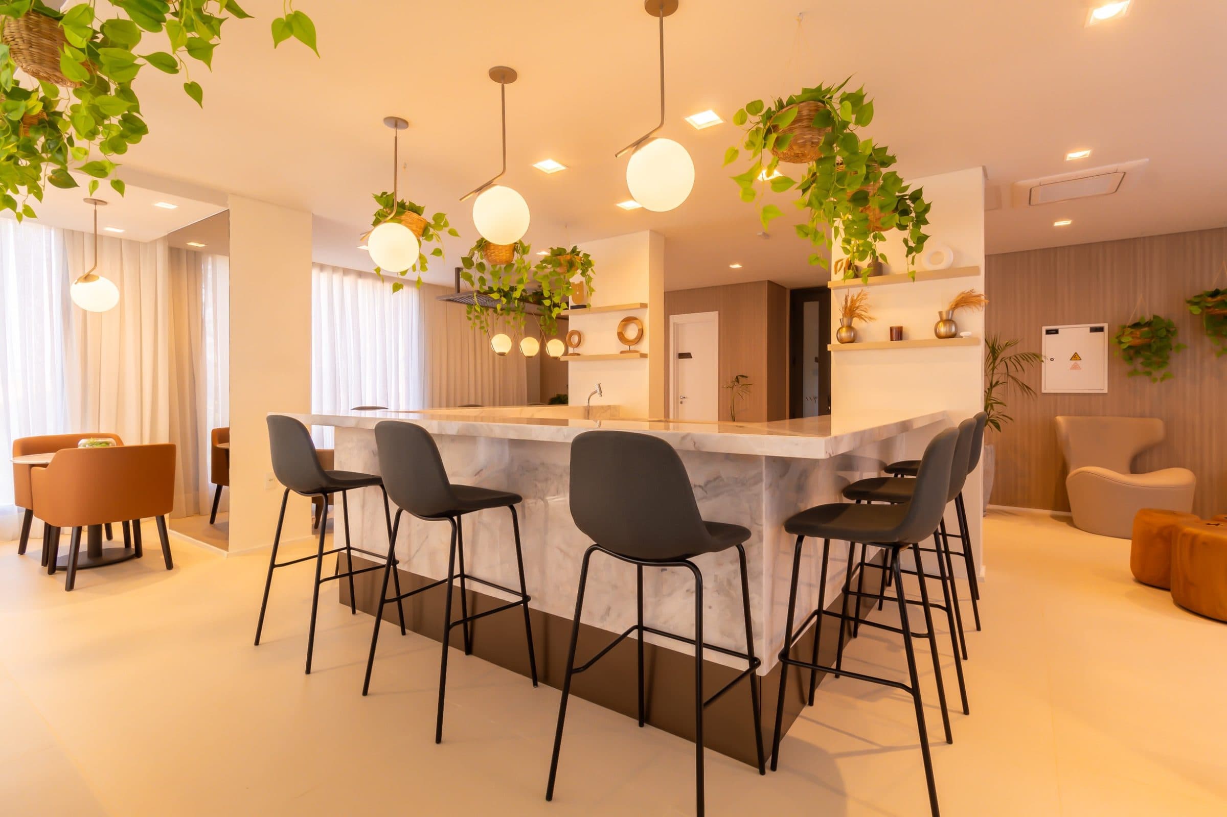 Área comum com bancada em mármore, banquetas e luminárias pendentes