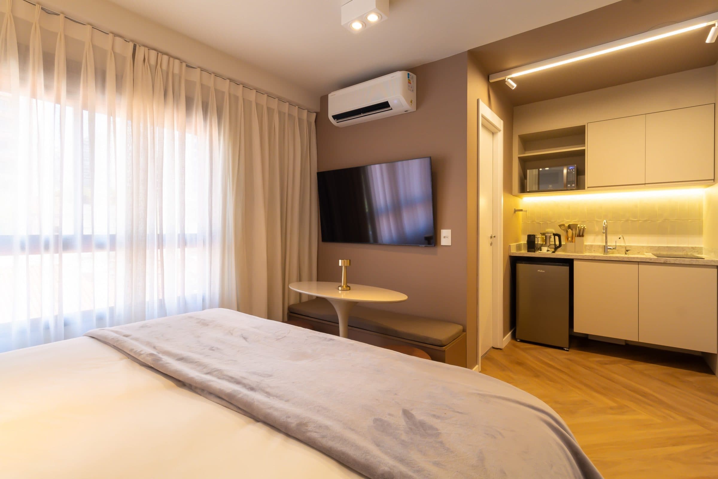 Studio com cama de casal, mesa de apoio e cozinha compacta integrada